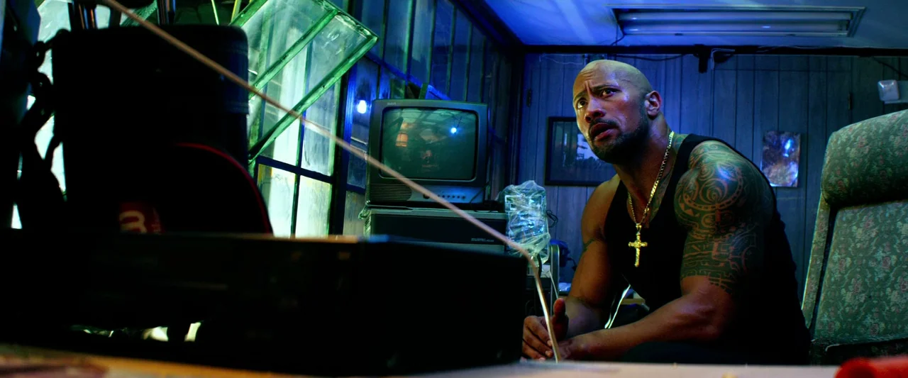 Pain & Gain (2013) movie still: medium — A dimly lit room features wood-paneled walls and old electronics arranged near windows. A bald man with a…