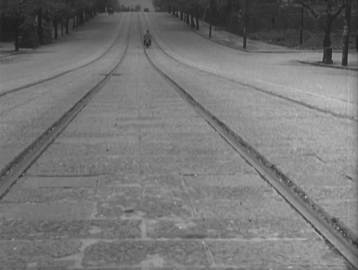 Scandal (1950) movie still: wide — A long, deserted street paved with stone is bisected by parallel sets of tram tracks. A lone figure on a…
