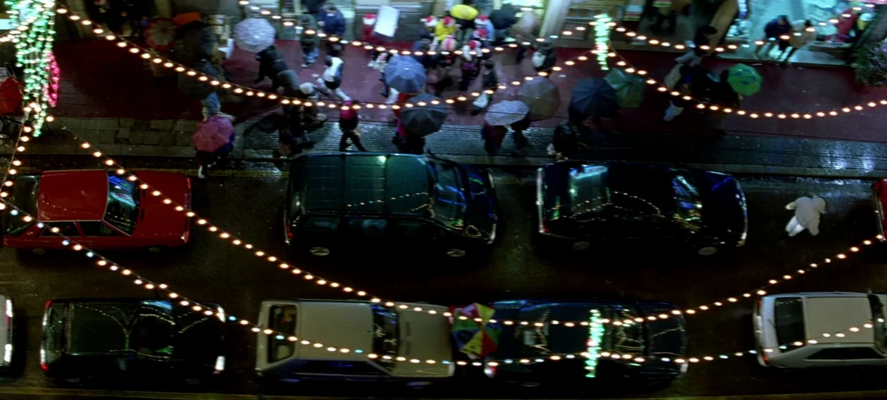 Live Flesh (1997) movie still: establishing — A rain-slicked city street at night is viewed from a high top-down perspective. Multiple parked cars…