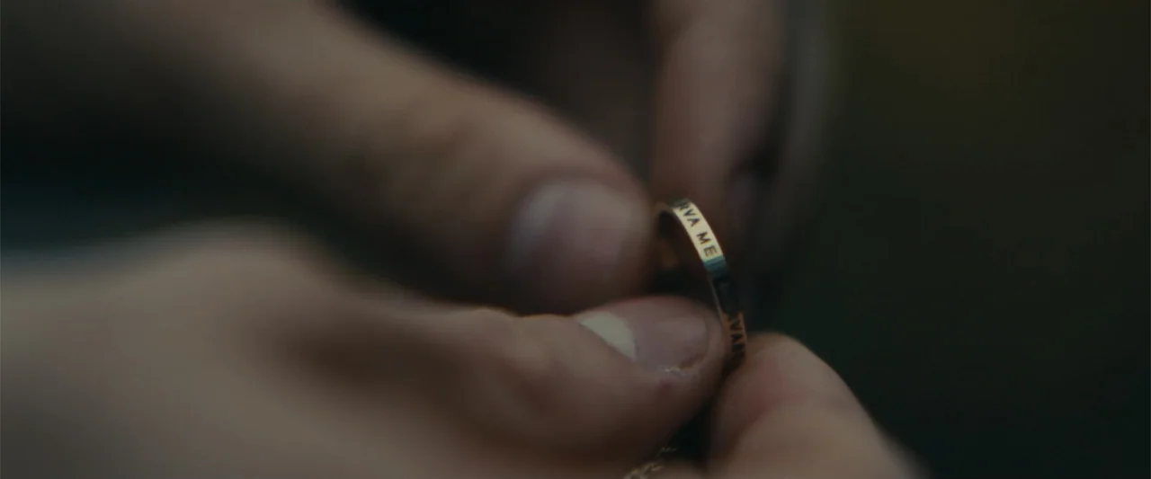 Chemical Hearts (2020) movie still: closeup — A close-up view shows two hands holding a thin gold ring with lettering. The focus remains strictly on…