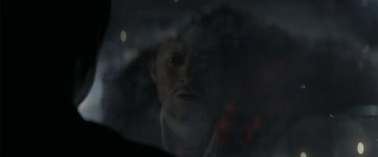 Godzilla (2014) movie still: closeup — A man's face appears as a reflection on a dirty window pane at night. The foreground silhouette of a person…