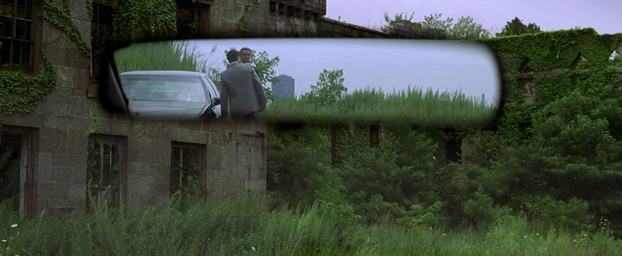 The Yards (2000) movie still: wide — An abandoned stone building covered in climbing ivy sits amidst tall, unkempt green weeds. A reflection in a…
