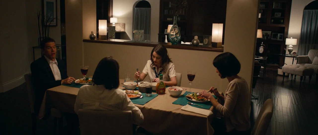 The Purge (2013) movie still: wide — A dining area contains a table covered in a tan cloth with place settings. Four individuals sit around the…
