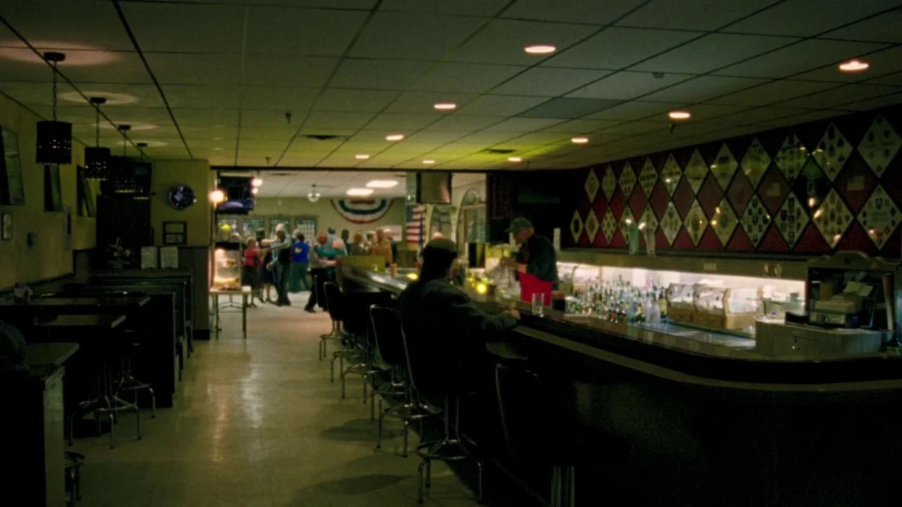I Am Not a Serial Killer (2016) movie still: wide — A dimly lit lounge with drop ceiling tiles and a long wooden service bar. Patrons dance in the…