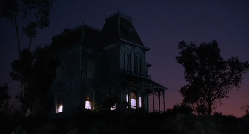 Psycho 2 (1983) movie still: establishing — A dark two-story Victorian mansion sits on a hill against a darkening twilight sky. Warm light emanates…