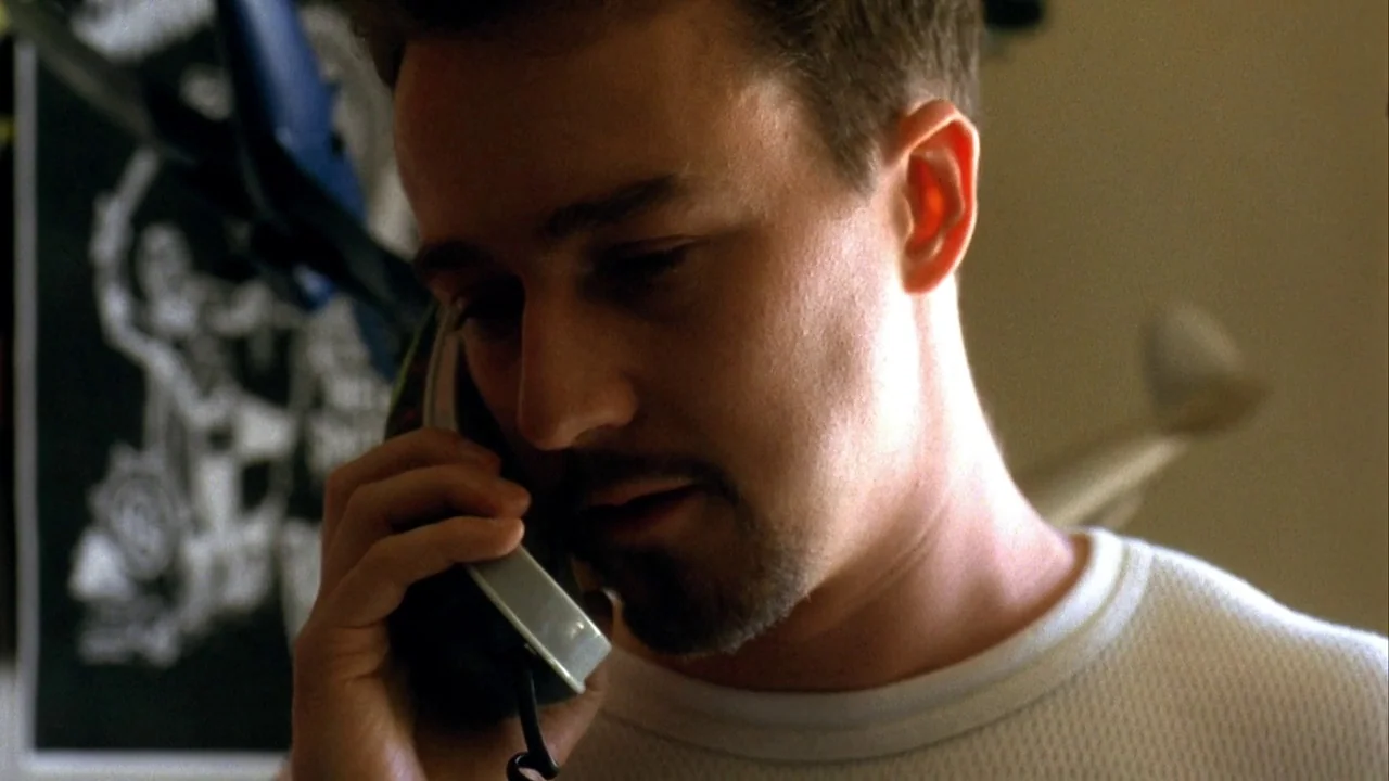 American History X movie still: closeup — A dimly lit room contains a person engaged in a private telephone call. The subject holds a classic…