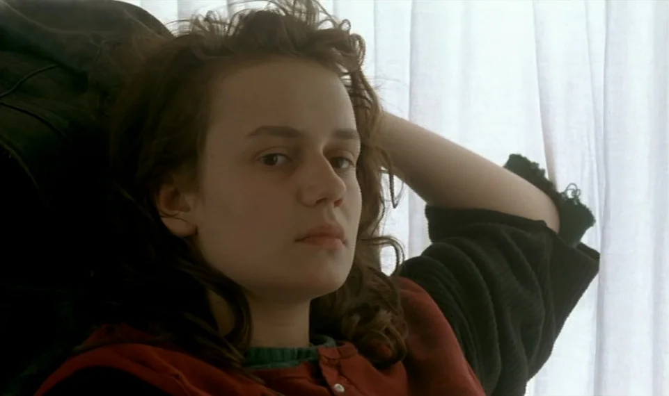 Vagabond (1985) movie still: closeup — A person rests against a surface in front of white vertical blinds. The individual looks directly forward…