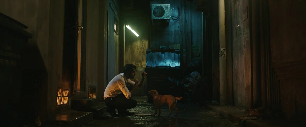 Monkey Man (2024) movie still: fullbody — A narrow city alleyway features dark dumpsters, textured concrete walls, and an overhead air conditioner.…