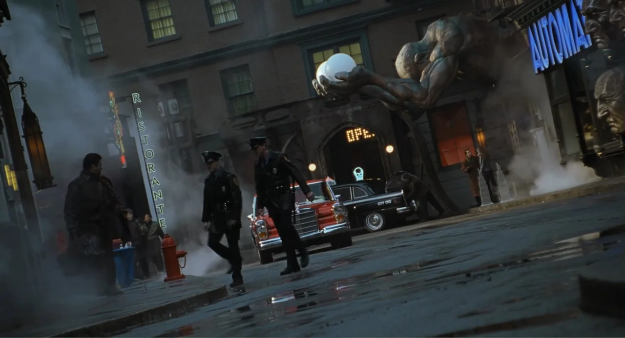 Batman & Robin (1997) movie still: wide — A dark, wet city street features a large stone sculpture of a hand holding spheres. Two police officers…