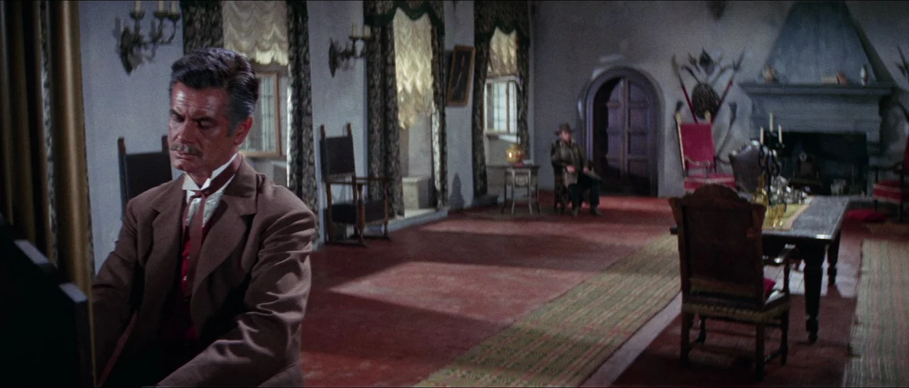 Texas, Adios (1966) movie still: medium — A spacious room contains heavy antique wooden furniture, patterned curtains, and a stone fireplace. One…