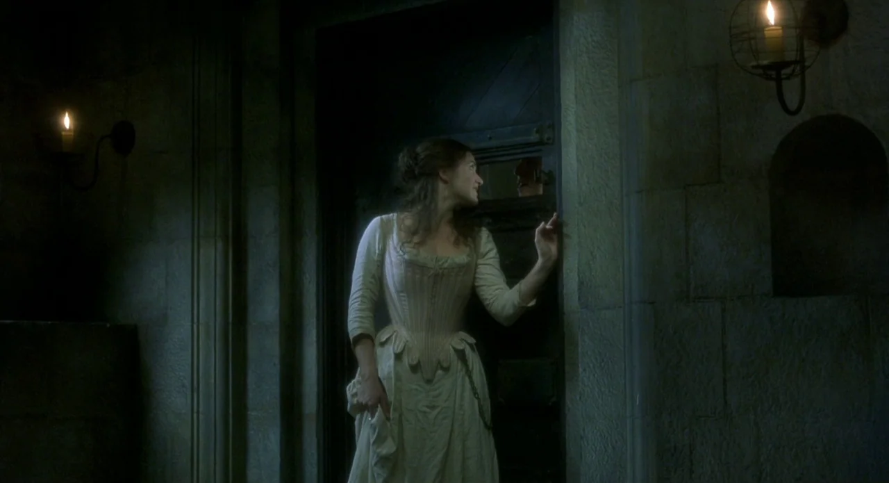 Quills (2000) movie still: medium — A stone corridor with dark, heavy doors lit by minimal candlelight in iron sconces. A young woman in a period…