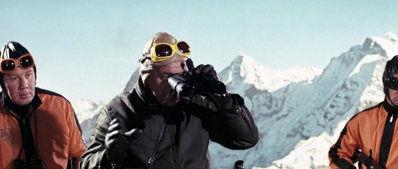 On Her Majesty’s Secret Service (1969) movie still: medium — A snowy mountain peak with rugged ice formations in the distant background. Three men…