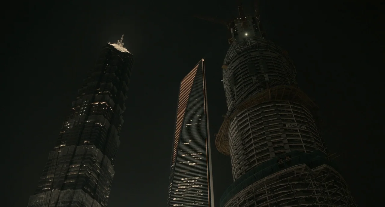 Her (2013) movie still: establishing — Three towering skyscrapers rise into the dark night sky above a dense city. One building is encased in…