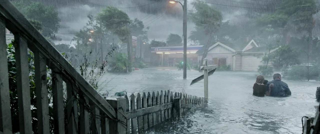 Crawl (2019) movie still: wide — A residential street is submerged in waist-deep water under heavy rain during a storm. Two people wade through the…