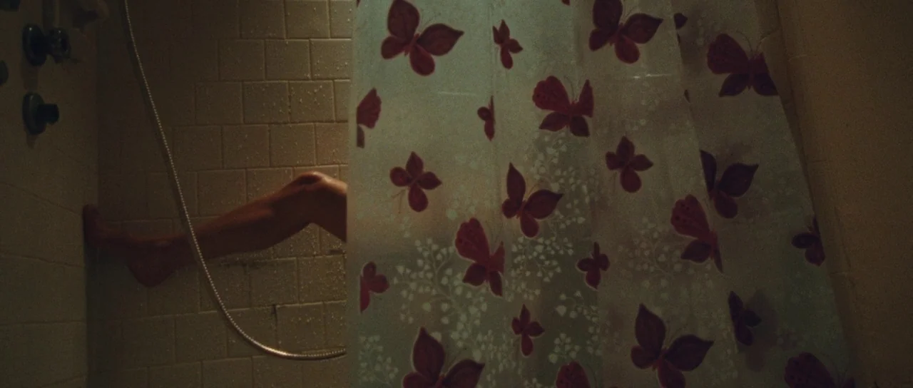 The Runaways (2010) movie still: medium — A tiled shower stall features a translucent white curtain decorated with repeating red butterflies. A…