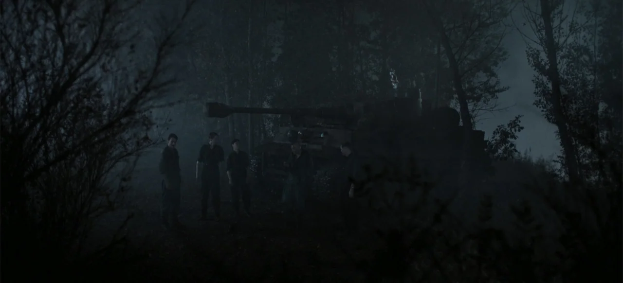 The Tank (2025) movie still: wide — A dark, misty woodland environment at night with tall, leafless trees and thick brush. Five soldiers stand near…