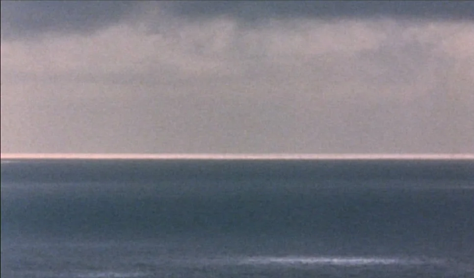 Heart of Glass (1976) movie still: establishing — A vast expanse of dark ocean meets an overcast sky at a clear horizon. A thin, bright line of…