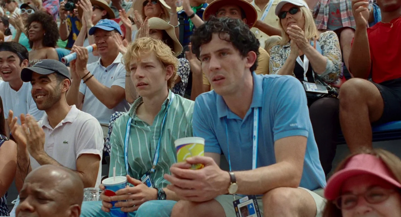 Challengers (2024) movie still: medium — Outdoor stadium bleachers filled with a diverse crowd of spectators during a daytime event. Two men sit in…
