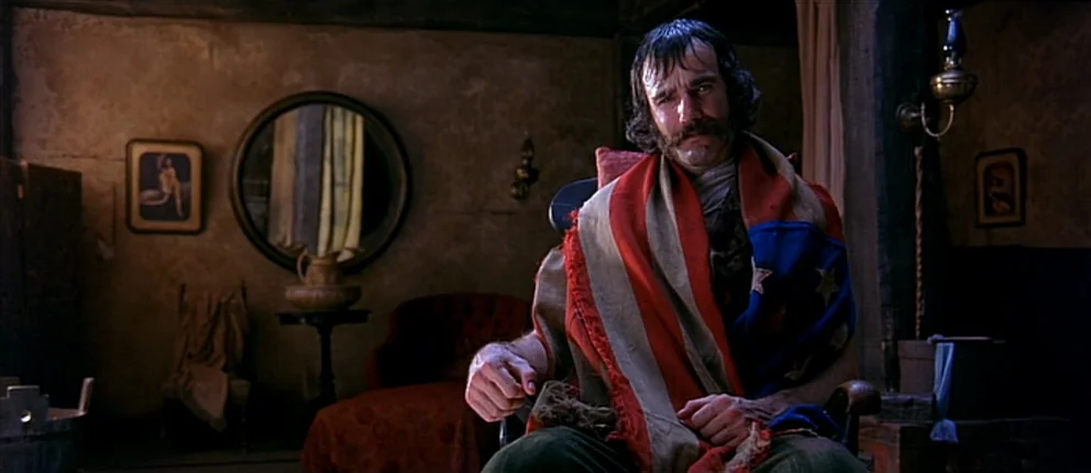 Gangs of New York (2002) movie still: medium — A dimly lit room features a round mirror and a small stool against walls. A man sits in a chair while…