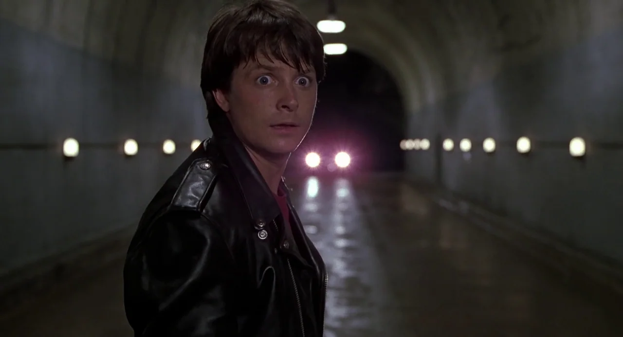 Back to the Future II (1989) movie still: medium — An arched concrete vehicle tunnel features lines of recessed lights on both side walls. A young…