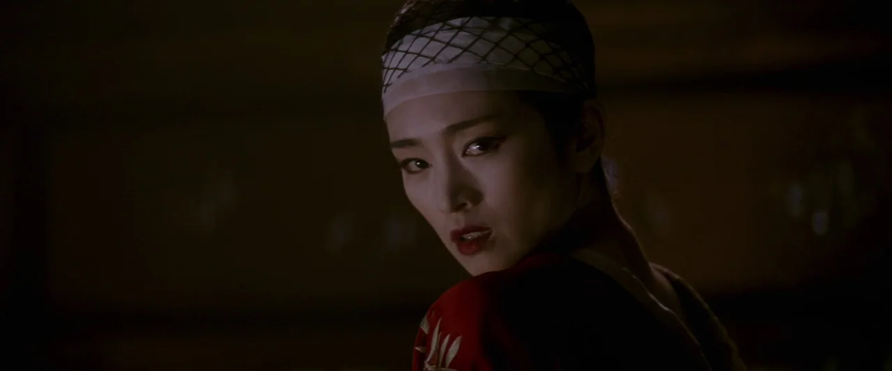 Memoirs of a Geisha (2005) movie still: closeup — A dark, minimally lit space provides a somber backdrop for a close-up shot. A woman with a head…