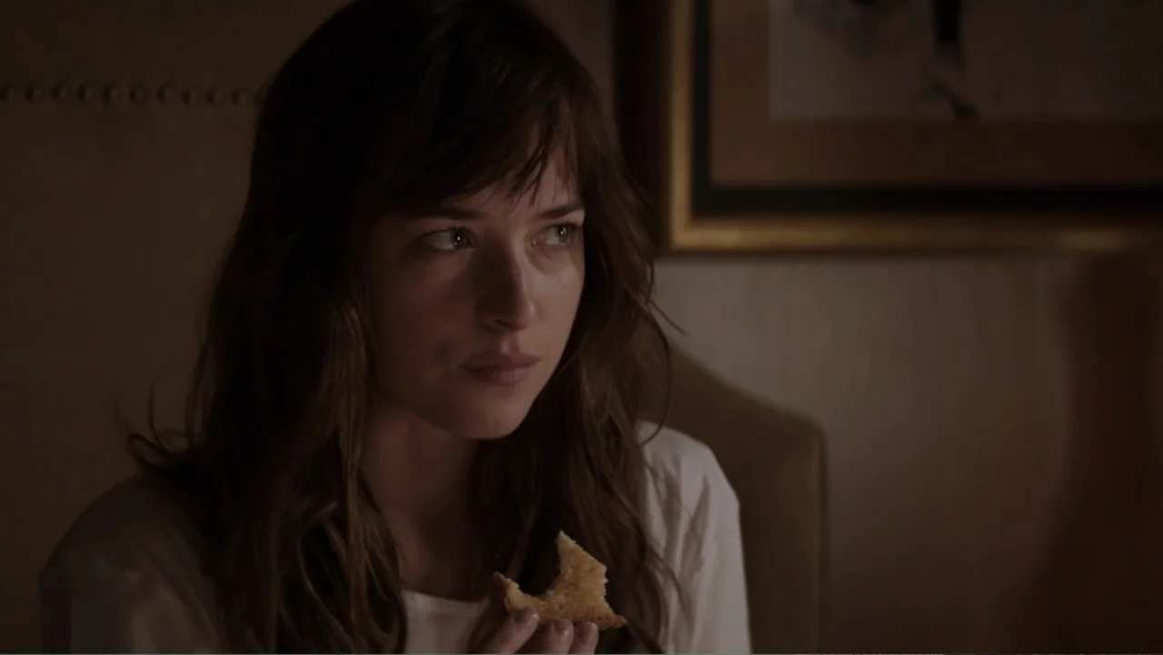 Fifty Shades of Grey (2015) movie still: closeup — A dimly lit interior room features a framed picture hanging on a wall. A young woman with dark…