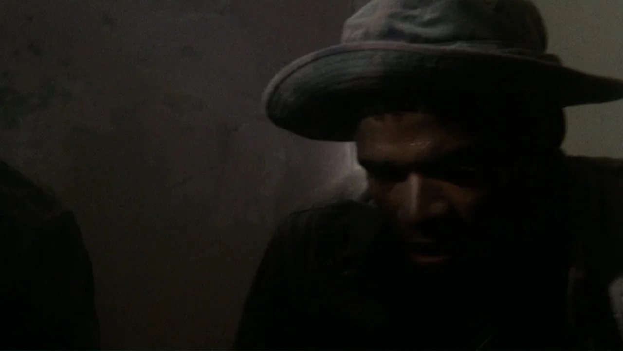 Heartbreak Ridge (1986) movie still: medium — A dimly lit indoor space with textured walls and minimal furniture visible. A man wearing a hat stands…