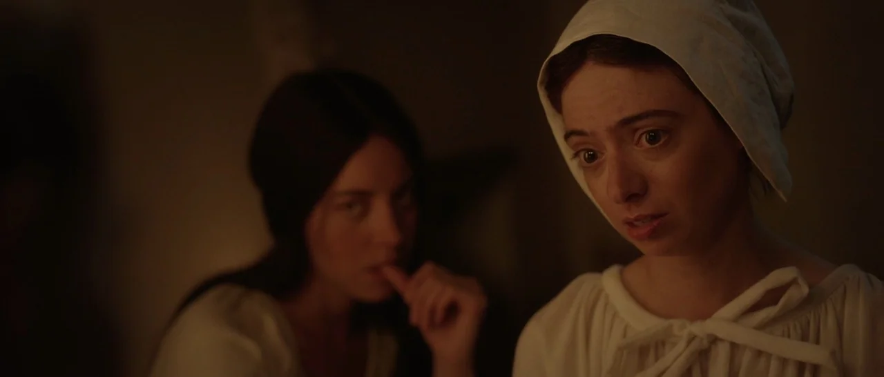 The Little Hours (2017) movie still: medium — A dark indoor space contains two women dressed in period-specific white clothing and bonnets. The…