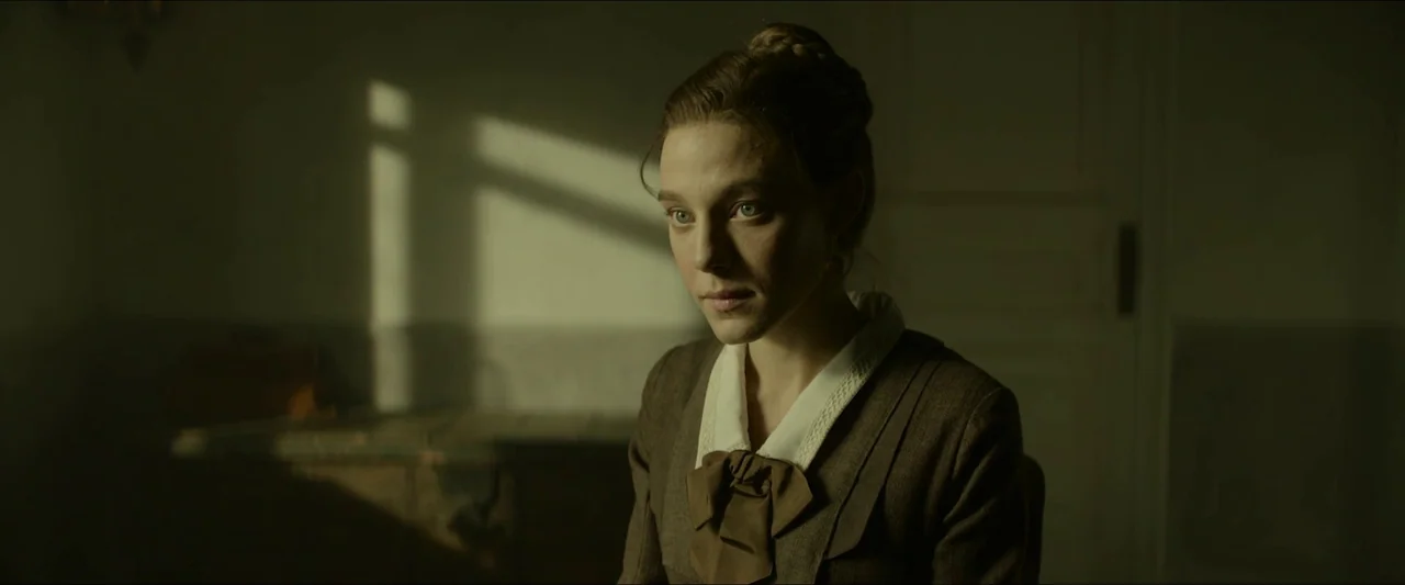 Tchaikovsky’s Wife (2022) movie still: medium — A dimly lit room with simple walls and a single window to the left. A woman wearing a…