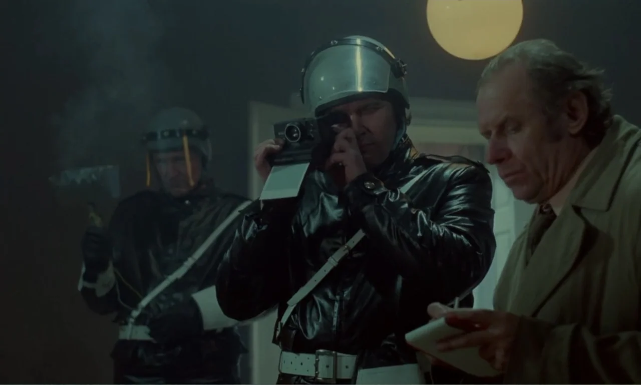 Ga-ga: Glory to the Heroes (1986) movie still: medium — A dimly lit interior room serves as a site for investigative police work. Two officers in…