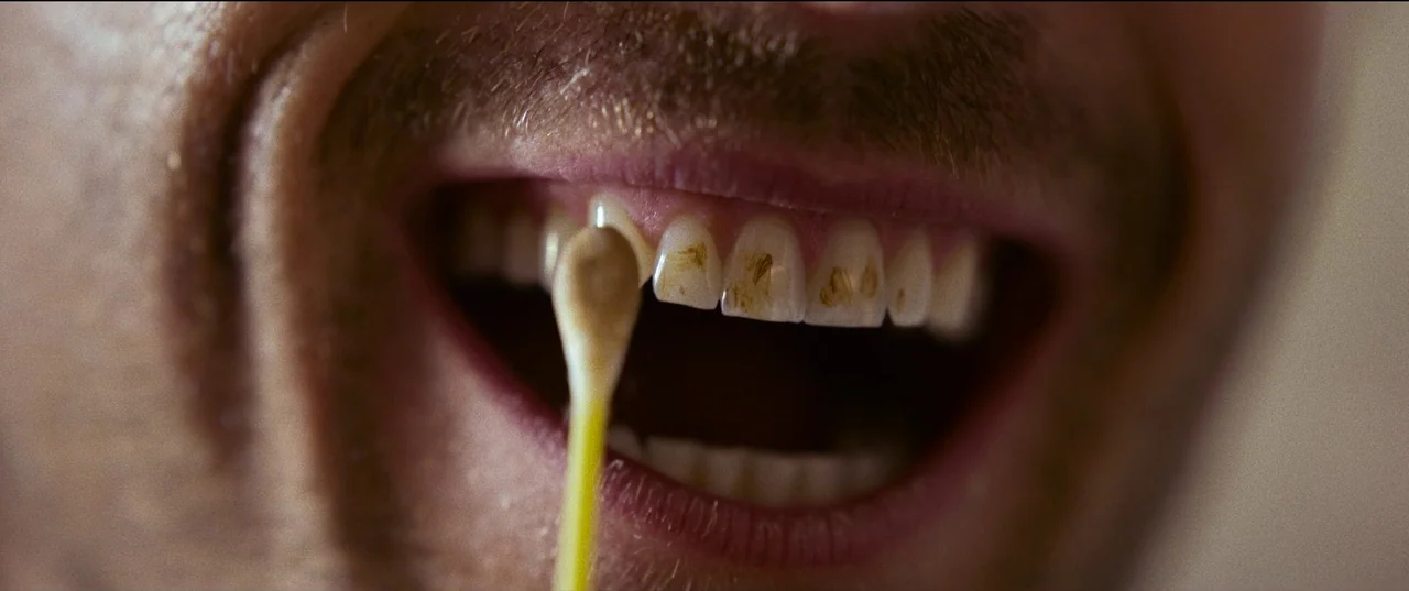 Hit Man (2023) movie still: closeup — A close-up view shows a person's open mouth and teeth in detail. A cotton swab is applied to the upper incisors.