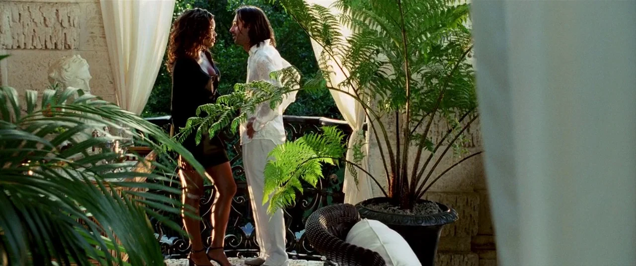 Bad Boys II (2003) movie still: fullbody — A sunny stone balcony features sheer white curtains and lush potted ferns in terracotta. A couple stands…
