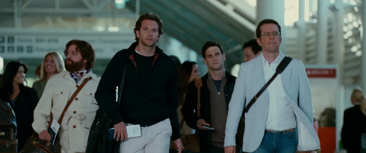 The Hangover Part II (2011) movie still: fullbody — An airport terminal with large arched support beams and overhead signage. Three men walk…