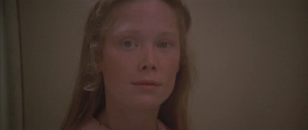 3 Women (1977) movie still: closeup — A close-up shot focuses on a young woman set against a plain beige wall. The girl looks directly toward the…