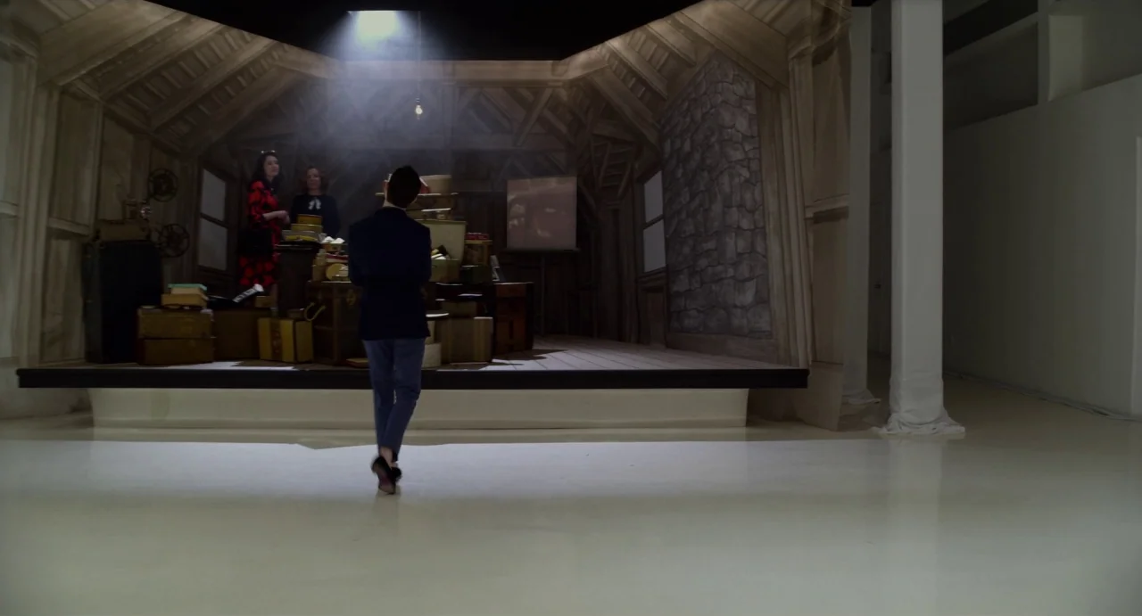 Velvet Buzzsaw (2019) movie still: wide — A person walks toward a raised set with a painted wooden backdrop on a stage. The set is filled with…