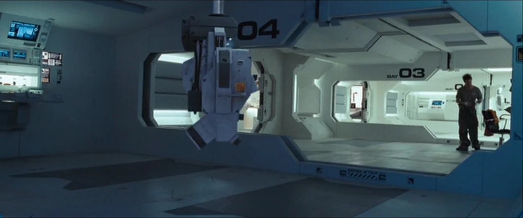 Moon (2009) movie still: wide — A sterile, white spaceship interior features modular wall sections labeled with industrial numeric indicators. A…