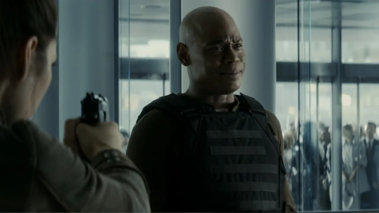 Total Recall (2012) movie still: medium — A modern building lobby features glass panels and a blurred crowd in the background. A woman holds a…
