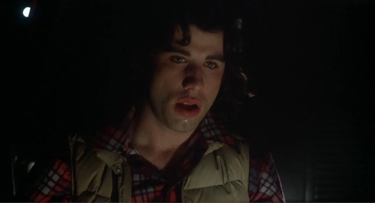 Carrie (1976) movie still: closeup — A dark, underexposed interior space surrounds a man seen in a tight close-up. The subject looks ahead with his…