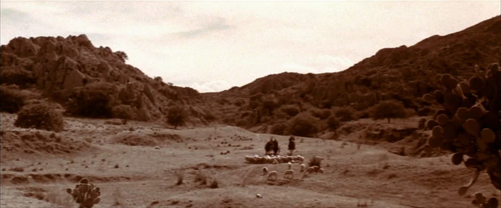Pat Garrett & Billy The Kid (1973) movie still: wide — An arid, rocky canyon landscape features scattered cacti and sparse low-lying vegetation. Two…
