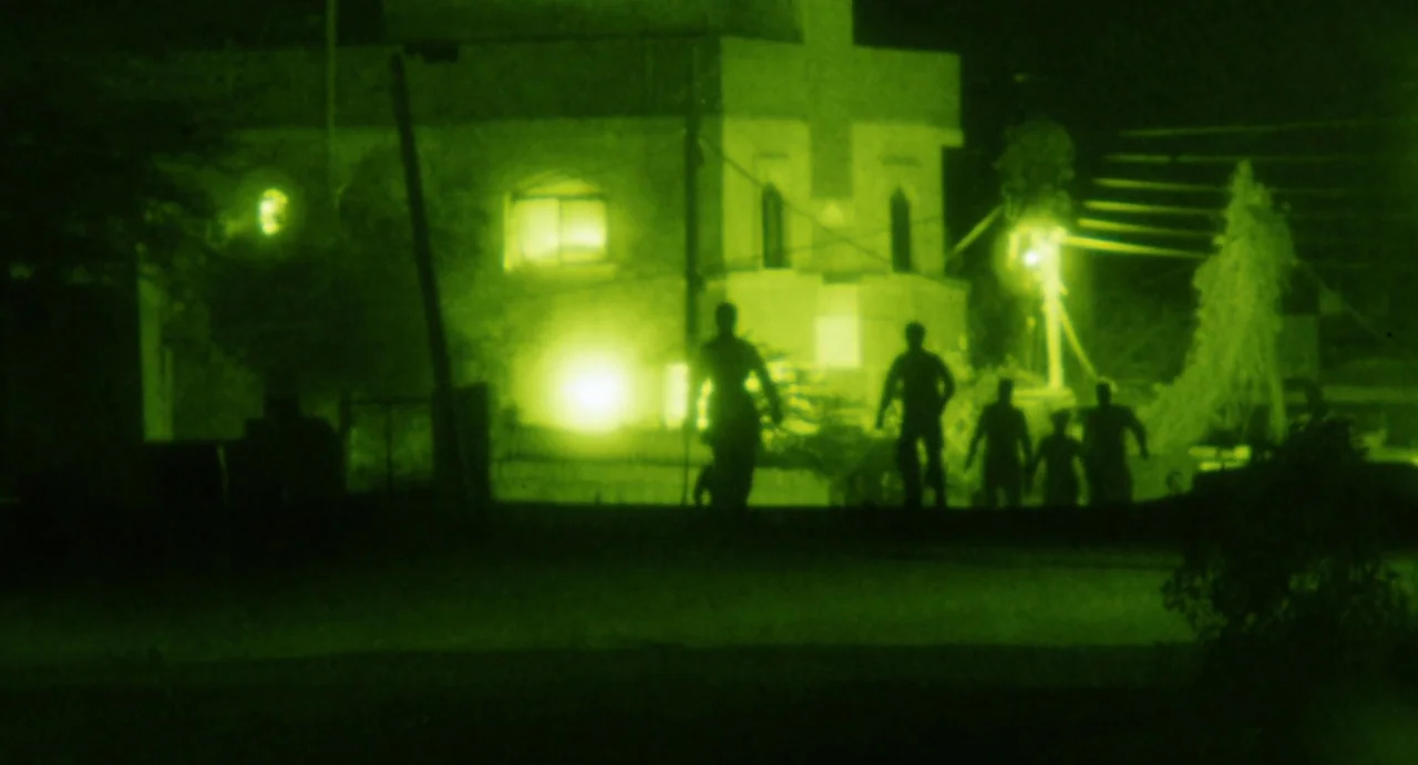 Zero Dark Thirty (2012) movie still: wide — A suburban residential exterior is shown at night through monochrome night vision optics. Several…