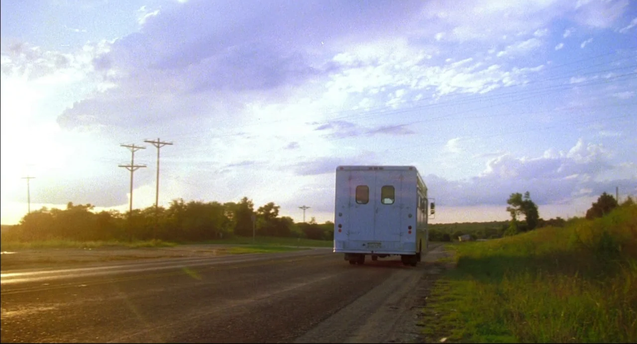 The Texas Chainsaw Massacre 2 (1986) movie still: wide — An asphalt road cuts through a rural landscape under a late afternoon sun. A white van…