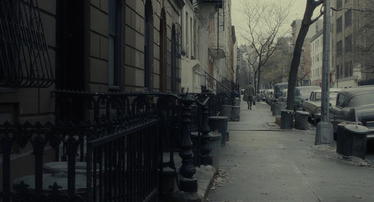 Inside Llewyn Davis (2013) movie still: wide — A sidewalk bordered by brownstone houses and vintage cars on a cloudy day. A man with a briefcase…