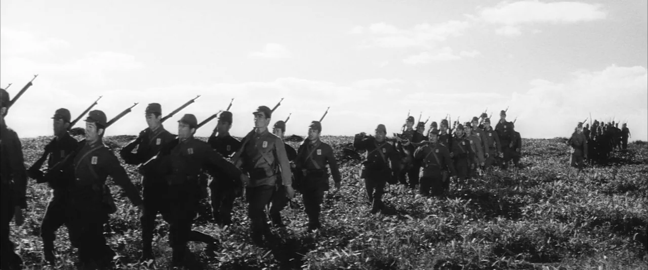 The Human Condition II: Road to Eternity (1959) movie still: wide — A line of Japanese soldiers marches across a wide, flat, grassy field under…