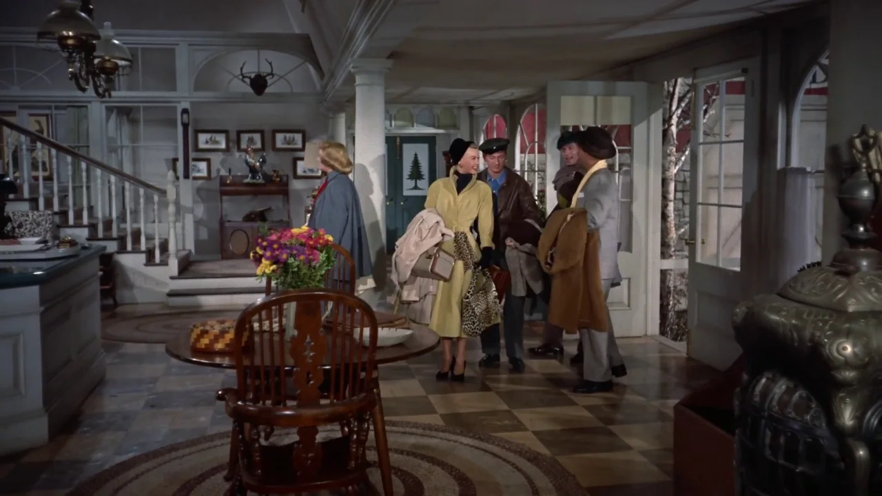 White Christmas (1954) movie still: wide — A spacious rustic lodge lobby with tiled flooring, wood accents, and large windowed doors. Four people in…