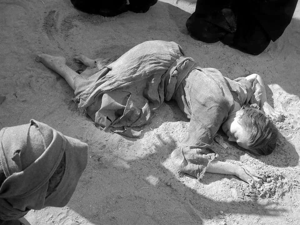 The Seventh Seal (1957) movie still: fullbody — A figure lies prostrate on a vast expanse of sun-drenched sand. The person is positioned in the…