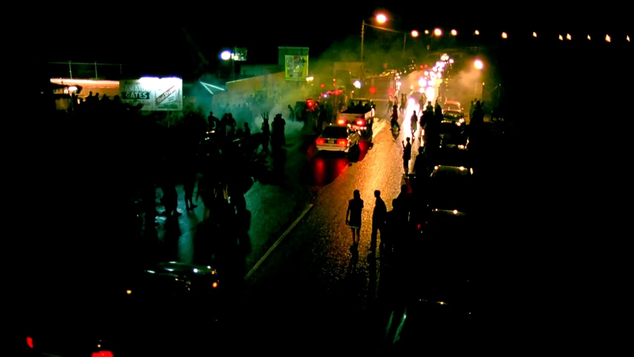 Belly (1998) movie still: wide — A dark urban street at night is filled with dense haze and numerous pedestrians. Vehicles move slowly through the…