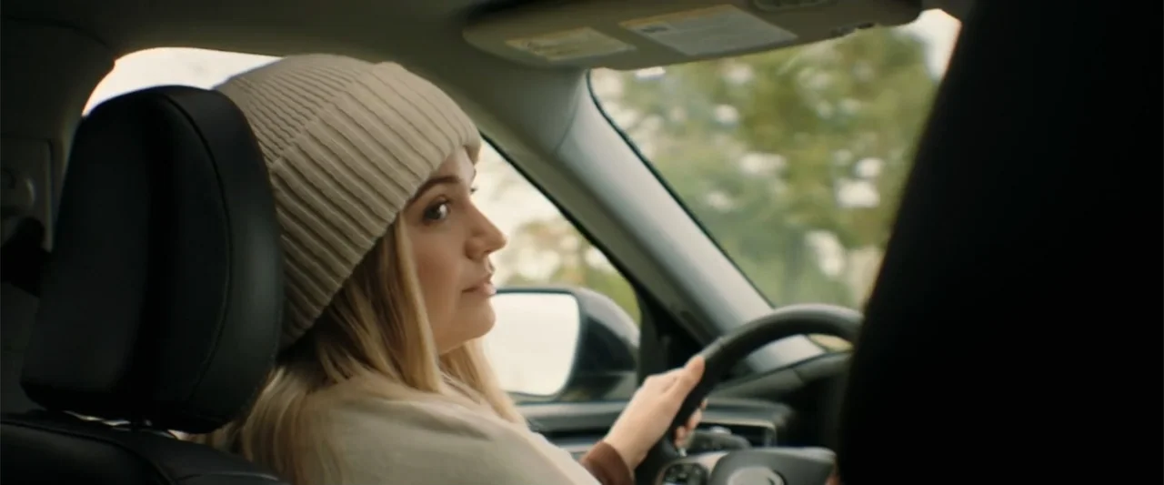Someone Like You (2024) movie still: medium — A modern car interior with dark leather headrests in the foreground. A young woman wearing a knit…