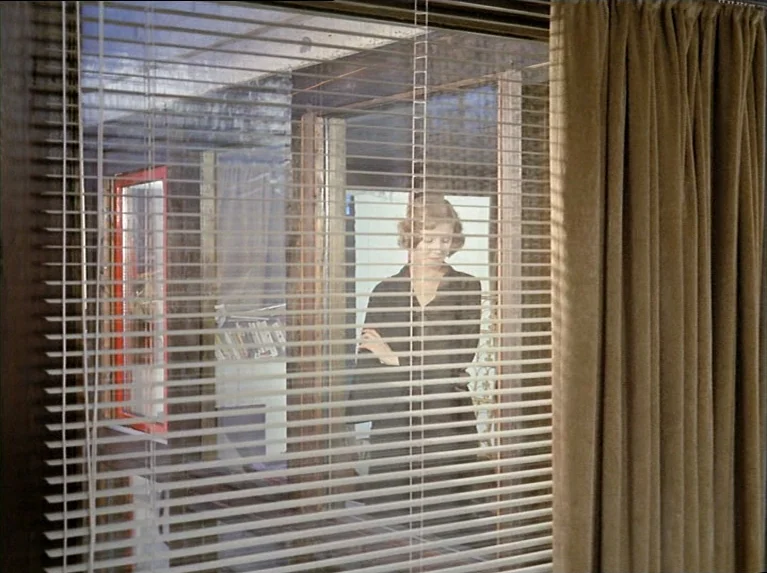 The Bitter Tears Of Petra Von Kant (1972) movie still: medium — A room viewed through horizontal window blinds and a partial fabric curtain. A woman…