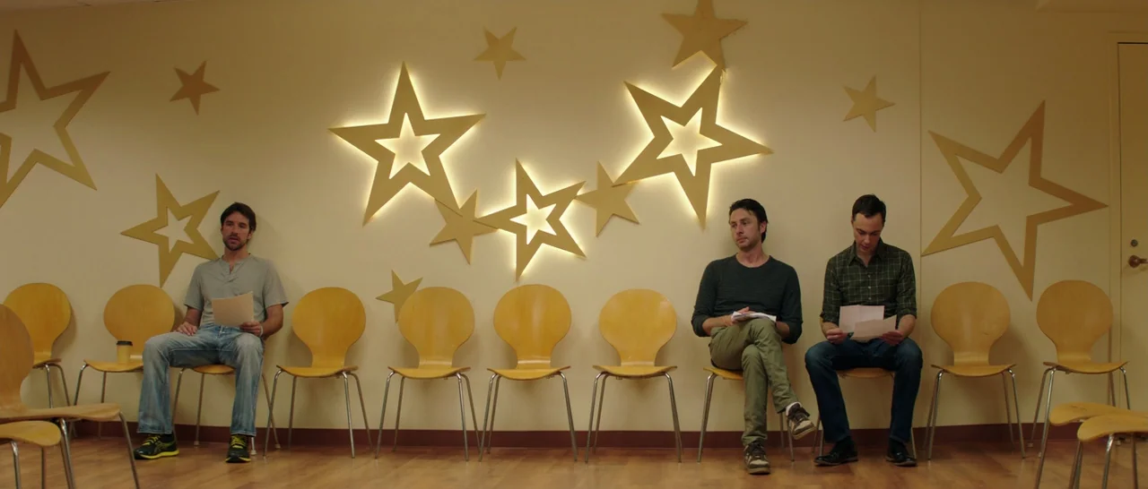 Wish I Was Here (2014) movie still: wide — A light-colored room features wooden chairs arranged along a wall decorated with illuminated star…