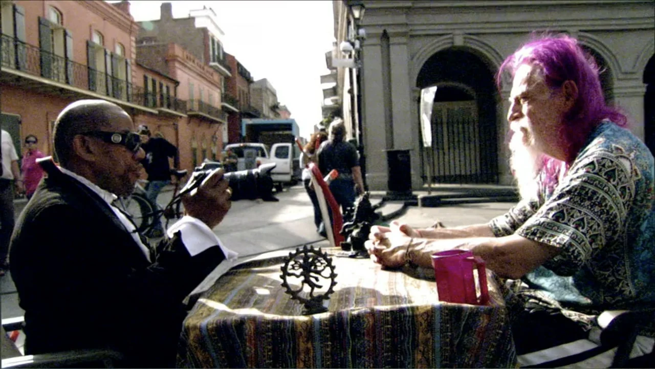 Dark Light: The Art of Blind Photographers (2009) movie still: medium — Two men sit at a small bistro table on a sunlit city street sidewalk. They…